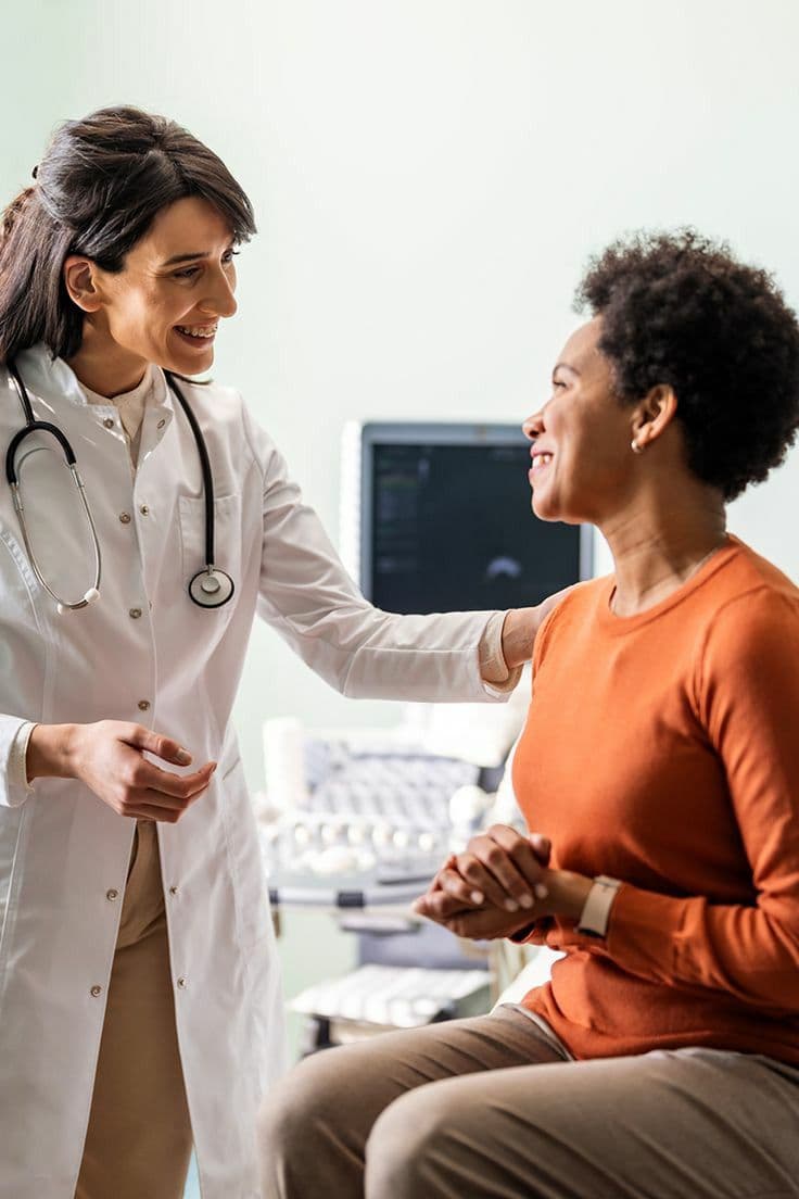 Médecin souriante posant la main sur l'épaule d'une patiente en consultation